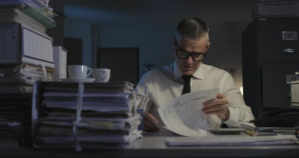 Stressed businessman working overtime overloaded with paperwork, he is rubbing his eyes