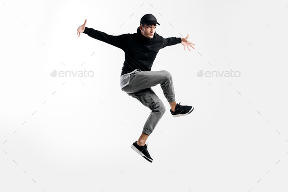 Handsome young dancer wearing a black sweatshirt, gray pants and a cap is dancing breakdance
