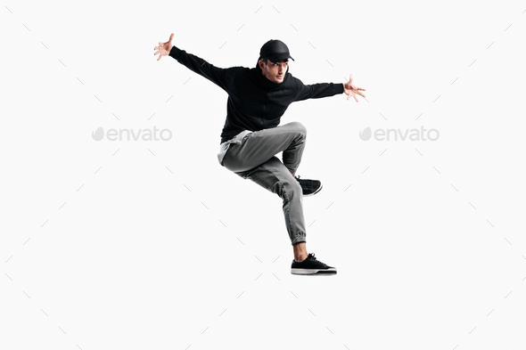 Stylish young man wearing a black sweatshirt, gray pants and a cap is dancing hip-poh