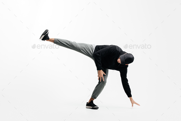 Handsome young man wearing a black sweatshirt, gray pants and a cap is dancing breakdance