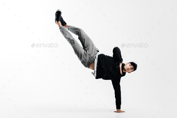 Stylish young man is dancing breakdance. He is standing on one arm and lifting both legs up