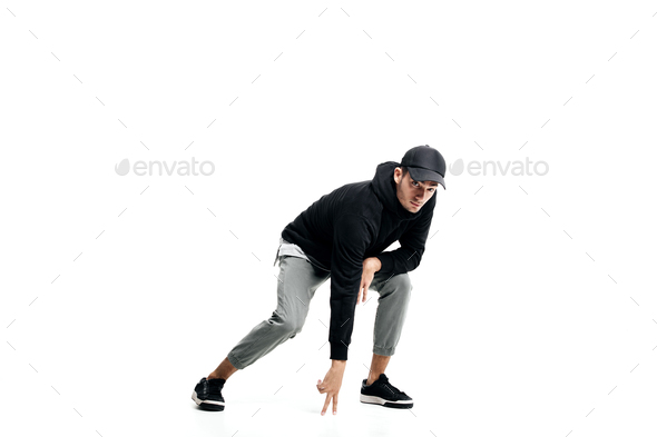 Young man wearing a black sweatshirt, gray pants, cap and sneakers dancing street dances on a white