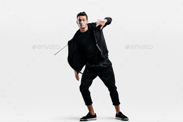 Stylish young man wearing a black sweatshirt and black pants makes stylized movements of hip-poh