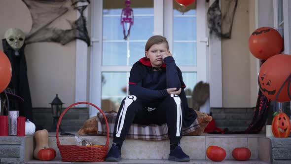 Wide Shot Sad Bored Caucasian Boy in Vampire Skeleton Costume Sitting on Porch Alone alt