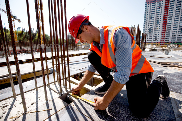 Man dressed in shirt, orange work vest and helmet measures the hole ...