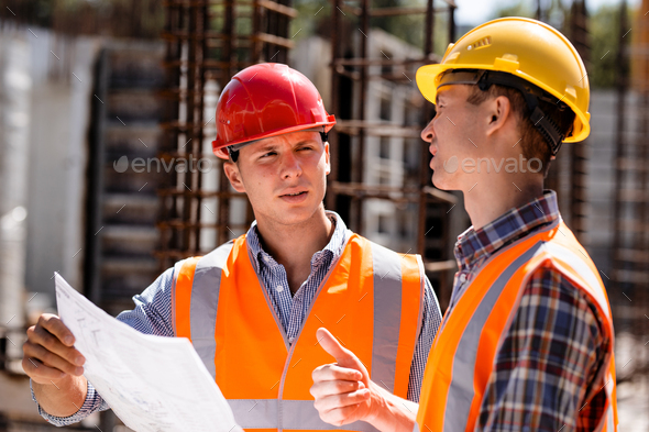 Civil engineer and construction manager in orange work vests and hard helmets explore construction
