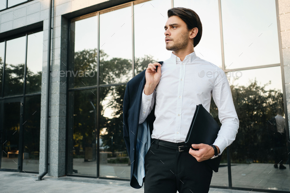Young handsome businessman in white shirt holding jacket on shoulder thoughtfully looking aside - Stock Photo - Images