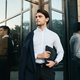 Young handsome man in jacket looking aside with bag for documents standing near glass building - PhotoDune Item for Sale