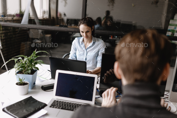Young woman and guy dressed in office style clothes are working at the laptops sitting at desks in