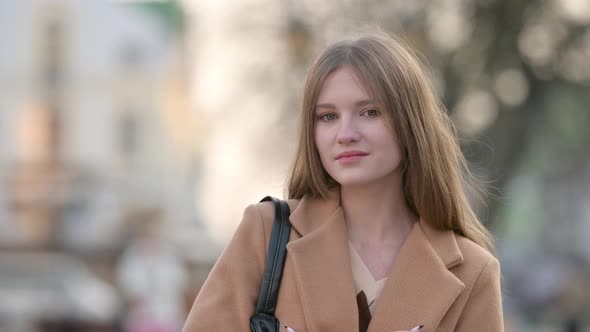 Attractive young lady in warm coat looking to camera on city street background.