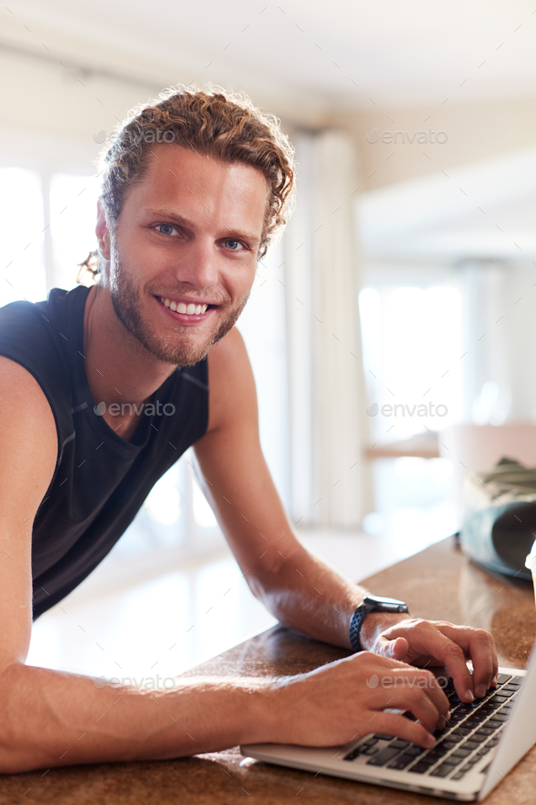 Millennial white man checking fitness app on laptop after a workout smiling to camera, vertical