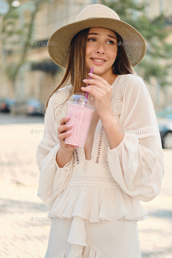 Young attractive woman in white dress and hat holding smoothie t