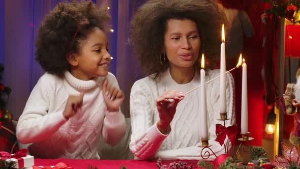 African American Mom and Little Daughter in White Sweaters Light Candles with Wow Delight Emotions alt