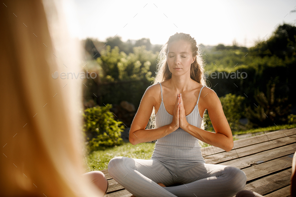 Young girl is sitting in the lotus position on a wooden podium in the garden in the sunny morning - Stock Photo - Images