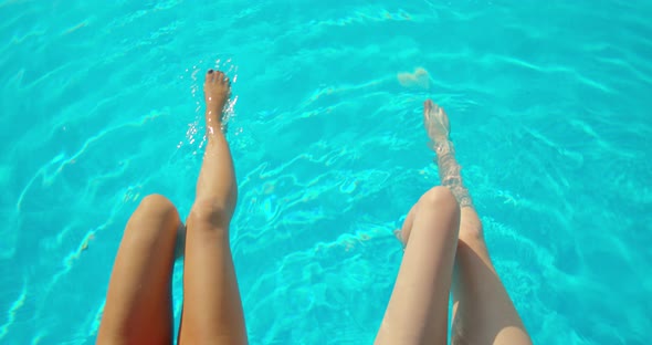 Young Women Sitting on Edge of Pool and Dangling Their Feet in Water. Two Girls with Slim Tanned alt