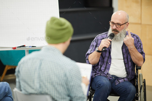 Confident senior man in wheelchair holding presentation for students - Stock Photo - Images