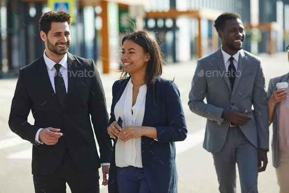 Positive multi-ethnic colleagues walking over street - Stock Photo - Images