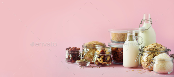 Glass bottles of vegan plant milk and almonds, nuts, coconut, hemp seed milk on pink background - Stock Photo - Images