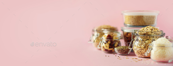 Vegan health food over pink background with copy space. Nuts, seeds, cereals, grains in glass jars - Stock Photo - Images
