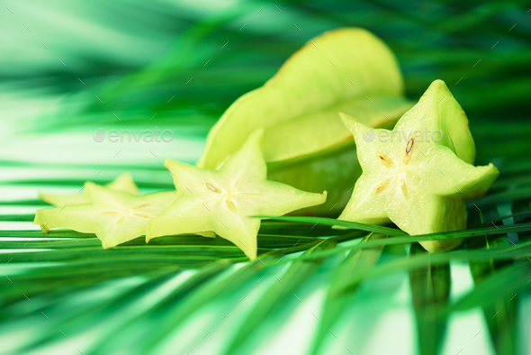 Exotic star fruit or averrhoa carambola over tropical green palm leaves on turquoise background - Stock Photo - Images