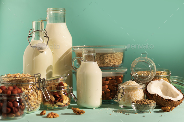 Vegan substitute dairy milk. Glass bottles with non-dairy milk and ingredients over blue background - Stock Photo - Images