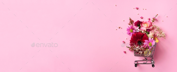 Shopping trolley with flowers on pink punchy pastel background. Banner with copy space. Top view - Stock Photo - Images