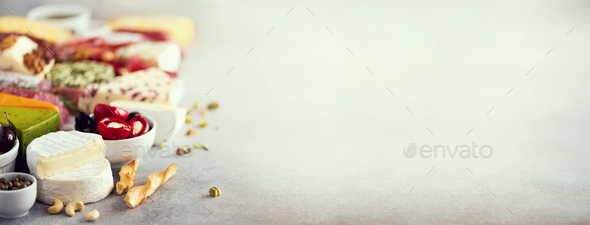 Assortment of hard, semi-soft and soft cheeses with olives, grissini bread sticks, capers, grape, on - Stock Photo - Images
