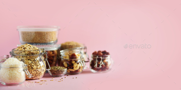 Grains, cereals, nut, dry fruits in glass jars over pink background with copy space. Clean eating - Stock Photo - Images