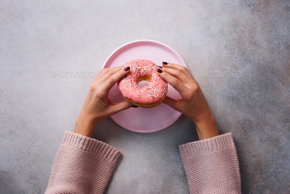 Female hands holding donut on pink plate over stone background. Top view, flat lay. Sweet, dessert - Stock Photo - Images