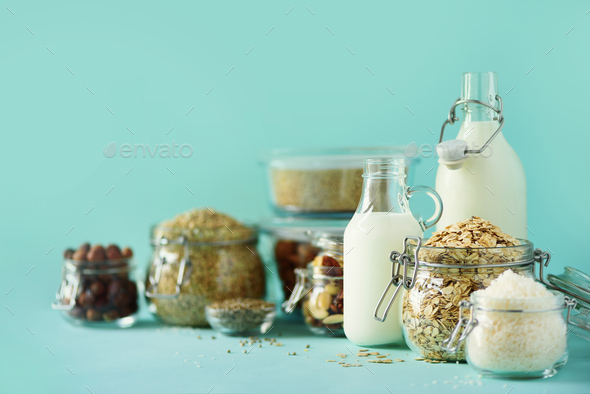 Vegan substitute dairy milk. Glass bottles with non-dairy milk and ingredients over blue background - Stock Photo - Images