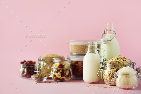 Vegan substitute dairy milk. Glass bottles with non-dairy milk and ingredients over pink background - Stock Photo - Images