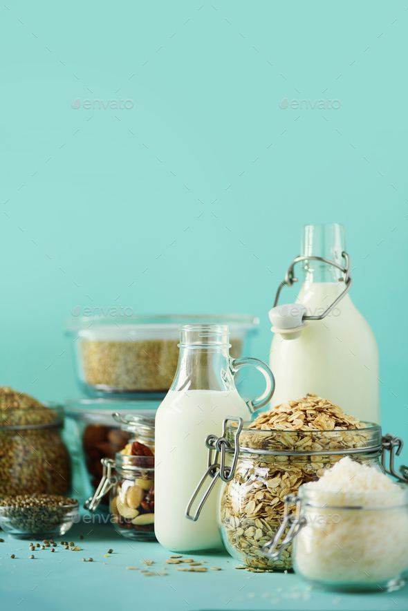 Glass bottles of vegan plant milk and almonds, nuts, coconut, hemp seed milk on blue background - Stock Photo - Images