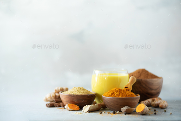Healthy vegan turmeric latte or golden milk, turmeric root, ginger powder, black pepper over grey - Stock Photo - Images