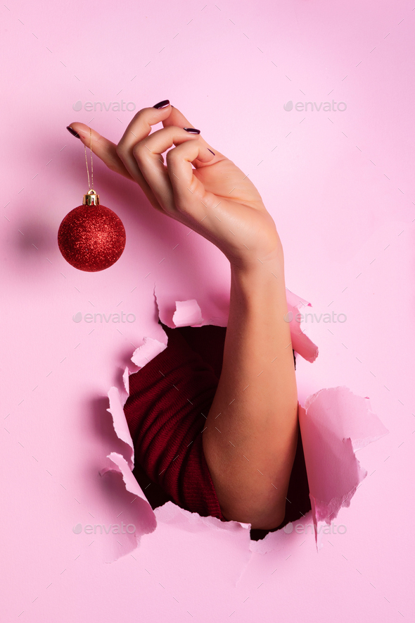 Woman holding red glittering Christmas ball in hand over pink background with snow, light bokeh - Stock Photo - Images