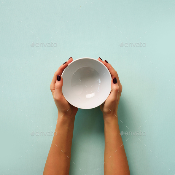 Female hand holding white empty bowl on blue background with copy space. Healthy eating, dieting - Stock Photo - Images