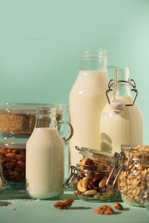 Glass bottles of vegan plant milk and almonds, nuts, coconut, hemp seed milk on blue background - Stock Photo - Images