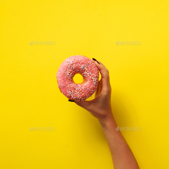 Woman hand holding delicious pink donut on yellow color background. Top view banner with copy space - Stock Photo - Images