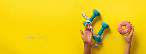 Female hand holding sweet donut, measuring tape, dumbbells over yellow background. Top view, flat - Stock Photo - Images