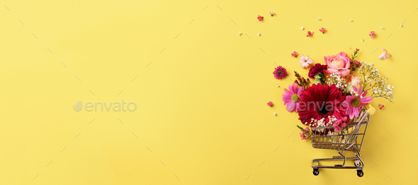 Shopping trolley with flowers on yellow punchy pastel background. Banner with copy space. Top view - Stock Photo - Images