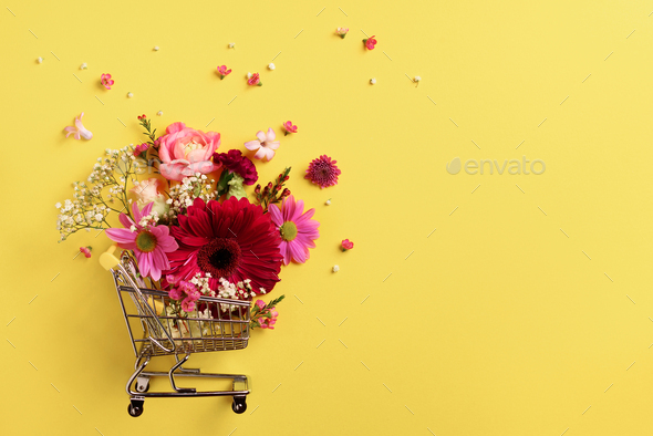 Shopping trolley with flowers on yellow punchy pastel background. Banner with copy space. Top view - Stock Photo - Images