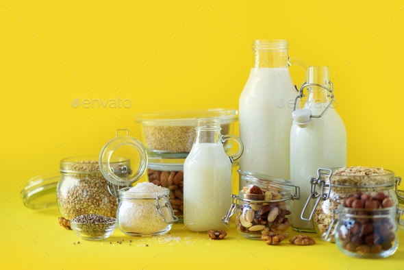 Glass bottles of vegan plant milk and almonds, nuts, coconut, hemp seed milk on yellow background - Stock Photo - Images