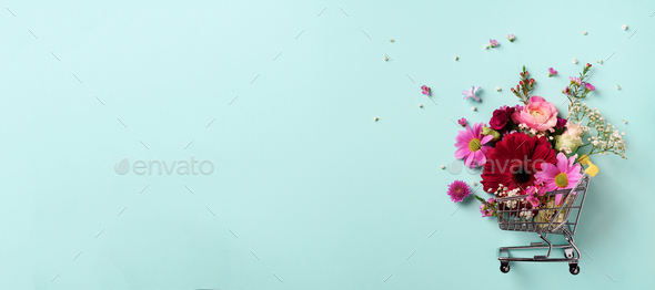 Shopping trolley with flowers on blue punchy pastel background. Banner with copy space. Top view - Stock Photo - Images
