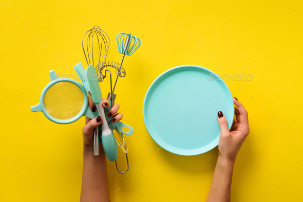 Woman hand holding kitchen utensils on yellow background. Baking tools - plate, brush, whisk - Stock Photo - Images