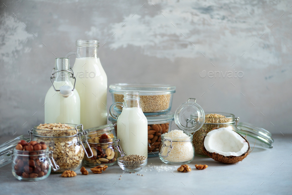 Glass bottles of vegan plant milk and almonds, nuts, coconut, hemp seed milk on grey concrete - Stock Photo - Images