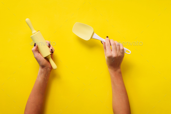 Woman hand holding kitchen utensils on yellow background. Baking tools - rolling pin, spatula - Stock Photo - Images