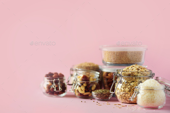 Grains, cereals, nut, dry fruits in glass jars over pink background with copy space. Clean eating - Stock Photo - Images