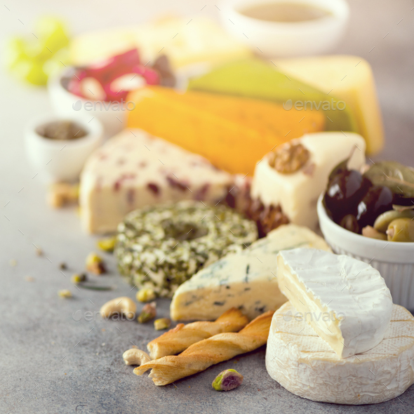 Assortment of hard, semi-soft and soft cheeses with olives, grissini bread sticks, capers, grape, on - Stock Photo - Images