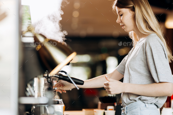 A good looking slim blonde with long hair,dressed in casual outfit,is cooking coffee in a modern - Stock Photo - Images