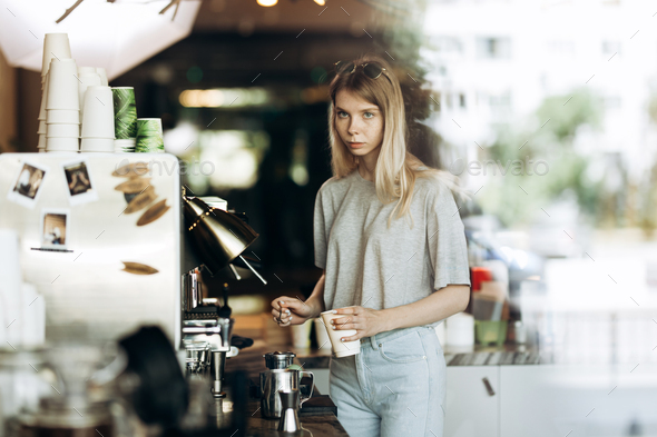 A young beautiful thin blonde with long hair,dressed in casual outfit,is cooking coffee in a modern