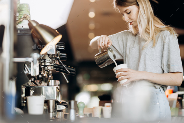 A good looking slim blonde with long hair,dressed in casual outfit,is cooking coffee in a modern - Stock Photo - Images